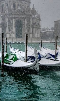 several gondolas in the water with snow falling on them and buildings in the background