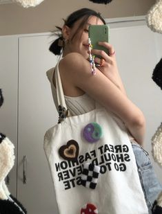 a woman taking a selfie in front of a mirror holding a cell phone and wearing a tote bag