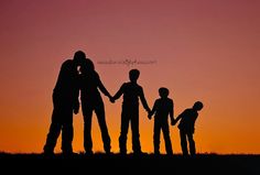 a family silhouetted against an orange and pink sky with the sun setting behind them