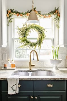 a kitchen sink under a window with wreaths on the windowsill and greenery