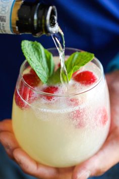 a person holding a wine glass filled with ice and raspberry spritz