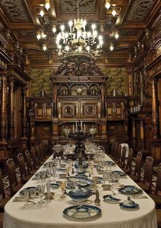 a long table is set up with plates and silverware in front of an ornate wooden paneled wall