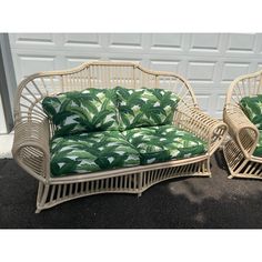 two wicker couches with green and white tropical print cushions, one is sitting on the ground