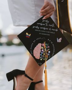 a woman in high heels holding a black graduation cap with an embroidered brain on it