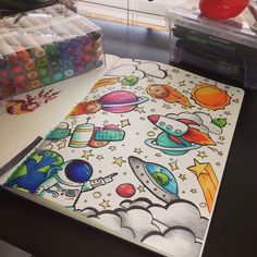 a coloring book with space and stars on it sitting on a desk next to markers