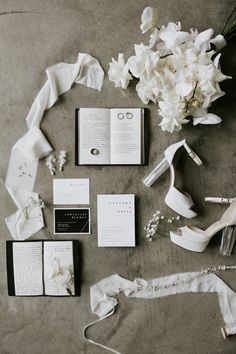 the wedding stationery is laid out on the floor next to flowers and shoes, including an open book