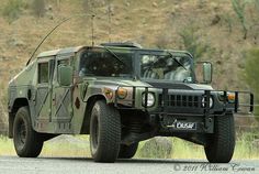 an army vehicle is parked on the side of the road in front of a hill