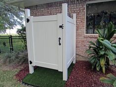 a white storage shed sitting in front of a brick house next to a lush green yard