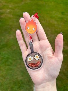 a hand holding a frying pan with bacon and an egg on it in front of a green lawn