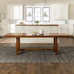 a large wooden table sitting in the middle of a kitchen next to white cupboards