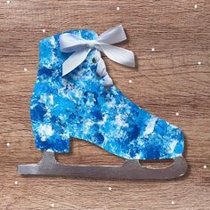 an ice skate ornament made out of blue and white paper on a wooden surface