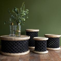 three black rope wrapped stools and a vase with flowers in it on a wooden table