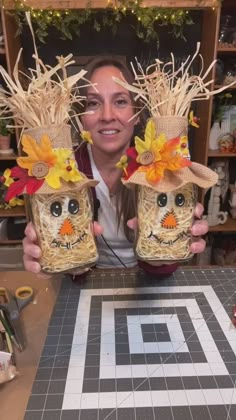 a woman is holding two jars decorated with flowers and scarecrows on their heads