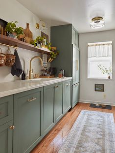 a kitchen with green cabinets and white counter tops on top of a wooden floor next to a window