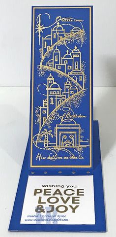 a blue and gold greeting card with an image of a town on it, the words peace love joy