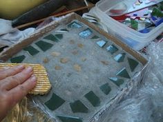 a person holding a sponge next to a box with some glass tiles on it and other items in the background