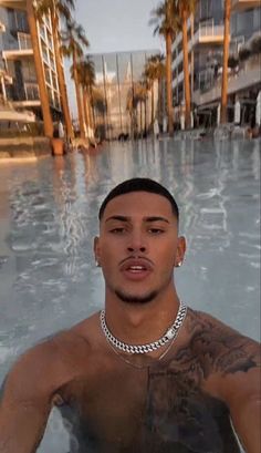 a man with tattoos standing in the middle of a swimming pool next to tall buildings