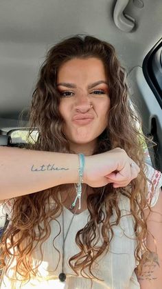 a woman sticking her tongue out in the back seat of a car, with tattoos on her arm