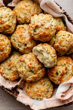 a basket full of biscuits and muffins sitting on top of a cloth covered table