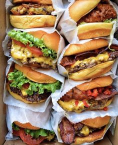 a box filled with lots of cheeseburgers covered in lettuce and bacon