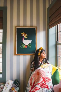 a woman sitting on top of a bed next to a window in a room with striped walls