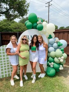 three women standing next to each other in front of a balloon arch with balloons on it