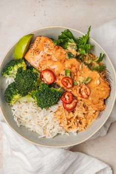 a white plate topped with rice, broccoli and fish next to a slice of lime