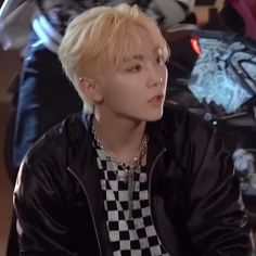 a man with blonde hair wearing a black and white checkered shirt sitting on a motorcycle