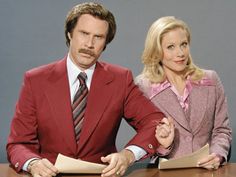 a man and woman sitting at a table with papers in front of them, posing for the camera