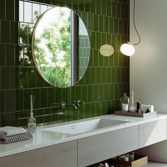 a green tiled bathroom with a round mirror above the sink and white countertop area