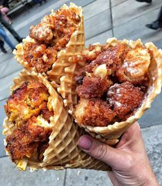 three waffles with meat and cheese on them are held up to the camera