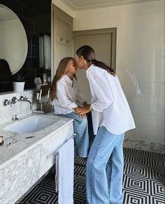 two women standing in front of a bathroom sink kissing each other's foreheads