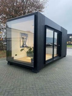 a large black container sitting on top of a brick sidewalk next to a tree and building