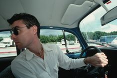 a man sitting in the drivers seat of a car with his hand on the steering wheel