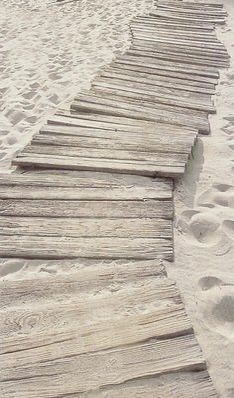 a wooden walkway on the beach with footprints