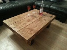 two glasses of wine sit on a wooden table in front of a black leather couch