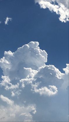 an airplane is flying in the blue sky with white fluffy clouds above it and below