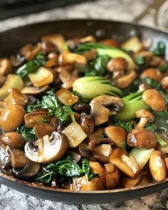 a pan filled with mushrooms and broccoli on top of a marble countertop