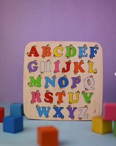 a wooden puzzle with letters and numbers on it next to colorful blocks in front of a purple wall