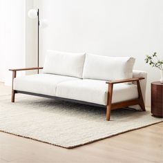 a white couch sitting on top of a wooden floor next to a lamp and potted plant