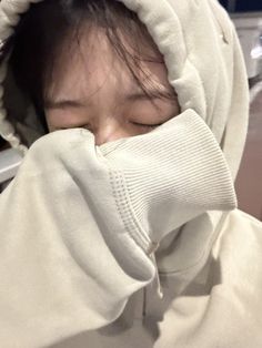 a woman with her eyes closed wearing a white hoodie over her head and covering her face