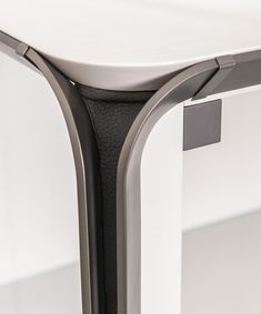 a close up view of the back end of a white table with metal legs and a black leather seat