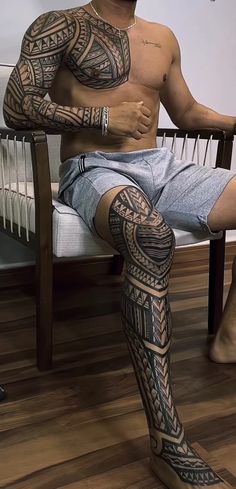 a man is sitting on a chair with his legs crossed and tattoos all over his body