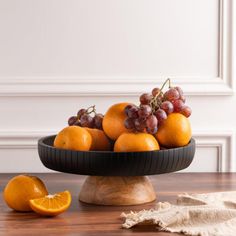 a bowl filled with oranges and grapes on top of a wooden table