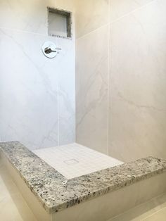 a bathroom with marble counter tops and white tile on the shower wall, along with a toilet paper dispenser