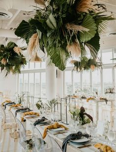 a long table is set up with clear chairs and greenery hanging from the ceiling