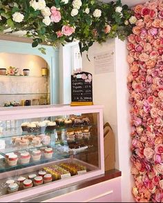 a display case filled with lots of cupcakes next to a flower covered wall