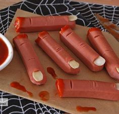 some hot dogs are on a cutting board with ketchup and a bowl of sauce