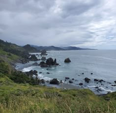 an ocean view with rocks and grass on the shore