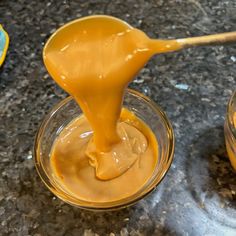 a spoon full of caramel sauce sitting on top of a glass bowl filled with liquid